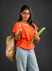 Poster - Beautiful young girl with a backpack standing and holding a notebook, posing on a grey background.