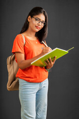 Poster - Beautiful young girl with a backpack standing and holding a notebook, posing on a grey background.