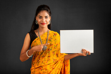 A young girl or businesswoman wearing a saree and holding a signboard in her hands on a gray background.