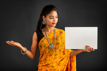 Wall Mural - A young girl or businesswoman wearing a saree and holding a signboard in her hands on a gray background.