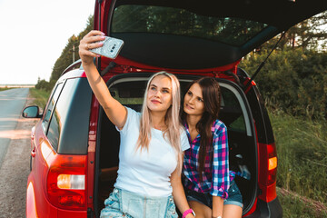 Sticker - Young pretty women friends travel by car. Summer holidays and active recreation. Positive emotions from the adventure, Girls take a selfie