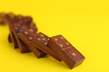 Wall Mural - Falling wooden domino tiles on yellow background, closeup