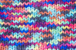 Woolen knitted background with a relief pattern. The texture of the fabric of a blanket or scarf is large. Wool, manual typewriter, handmade. Wildly Variegateds color. Knitted fabric as background