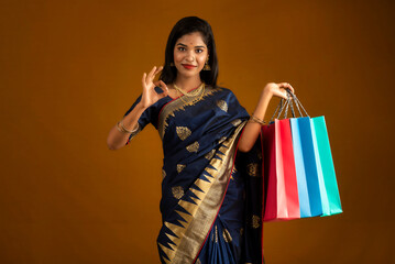 Poster - Beautiful Indian young girl or woman holding and posing with shopping bags on a brown background