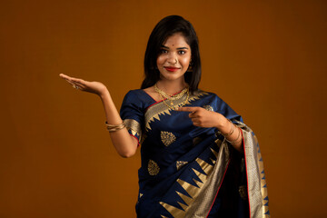 Sticker - Portrait of Indian traditional young woman or girl presenting something, showing copy space on her palm on a brown background