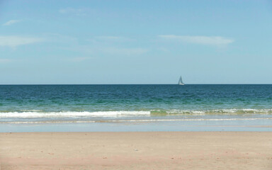 Breezy ocean view with clean sandy coastline and a boat on the horizon 