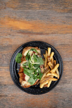 Top View Of A Gourmet Milanesa, Breaded Beef, Arugula And Mozzarella Cheese, And French Fries, In A Black Dish On The Restaurant Table.