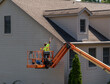 Workman painting the side of a townhouse while standing in an articulating boom lift