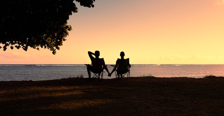 Silhouette of happy couple man and woman enjoying the nature sunset sitting holding hands 