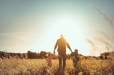 Father and his little children walking in a field into the sunset. Fatherhood, and family parenting concept. 