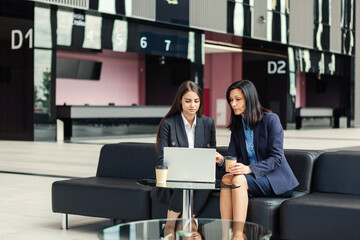 Wall Mural - Two businesswomen discussing project on laptop computer over coffee sitting in office lobby. Experienced mature entrepreneur mentoring and giving advice to young colleague