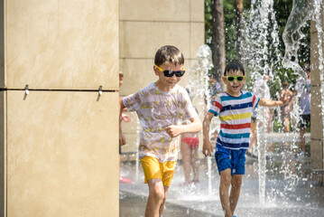 Boy having fun in water fountains. Child playing with a city fountain on hot summer day. Happy kids having fun in fountain. Summer weather. Active leisure, lifestyle and vacation