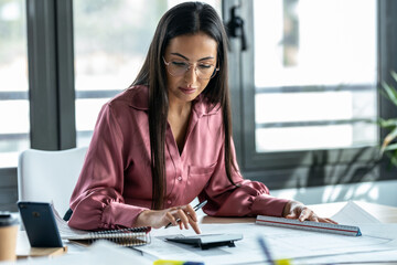 Concentrated young business woman working with blueprint in the office.