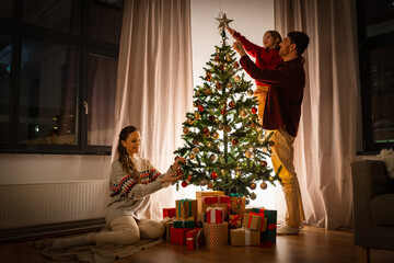 Poster - family, winter holidays and people concept - happy mother, father and little daughter decorating christmas tree at home