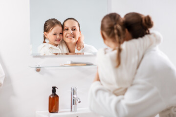 Sticker - beauty, family and people concept - happy smiling mother and little daughter looking to mirror and hugging in bathroom