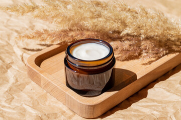 close up of collagen cream in open glass jar and dry flowers reeds on beige background. Set for skin and body care beauty products