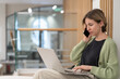 © DimaBerlin - Serious woman holding smartphone discussing project details while working online on laptop in coworking space, talking with client via cellphone, businesswoman with mobile phone looking at pc screen