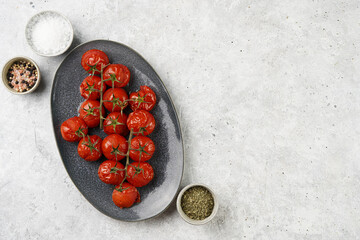 Roasted red tomatoes on branches on oval blue plate on grey background, top view, space for text