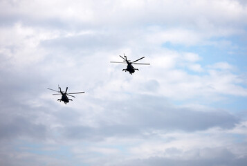 Silhouettes of two military helicopters Mi-8 in flight on background o blue sky and white clouds