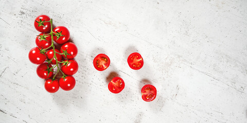 Poster - Vibrant small red tomatoes with green vines on white stone like board, view from above, empty space for text right side