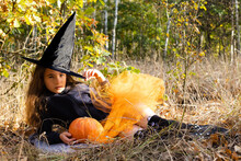 Little Girl Witch With Pumpkin In Hands In A Forest. Halloween Concept.