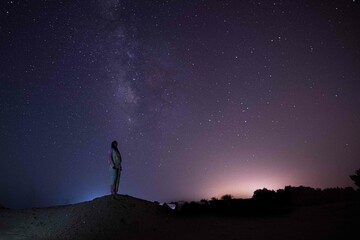 Wall Mural - milky way. night sky with stars and silhouette of a standing happy person with yellow and blue light