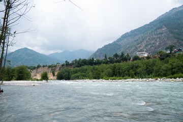 Scenic view of Beas river flowing in background of peaks of Himalayan mountains and dark clouds in sky at Manali, Himachal Pradesh, India. Mountain River. Travel in Himalayas. Natural landscape