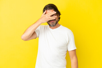 Wall Mural - Senior dutch man isolated on yellow background covering eyes by hands and smiling