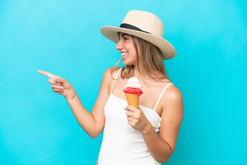 Wall Mural - Young caucasian woman in swimsuit with a cornet ice cream isolated on blue background pointing to the side to present a product