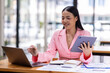 © David - Asian Businesswoman working in the workspace, doing report analyzing financial figures on a graph in tablet and sitting on laptop computer