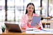 © David - Asian Businesswoman working in the workspace, doing report analyzing financial figures on a graph in tablet and sitting on laptop computer