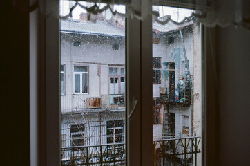 View through the window in a cold winter afternoon. Cozy and atmospheric old house in Lviv, Ukraine. Snowflakes flying from the sky. Film photography.