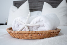 A View Of Bed Decor, Featuring A Basket, Rolled White Bath Towels And A Sea Star.