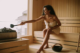 Young woman pouring water onto hot stone in the sauna