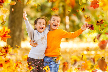 Wall Mural - Two little cute smiling kids in bright jackets walking together in a park on a sunny autumn day. Friendship between siblings. Happy family concept 