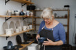 © ninelutsk - Potter artist showing her work in studio. Mature ceramist standing at workshop with clay cups in hands. Successful lady potter own making porcelain products