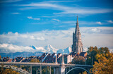 Fototapeta Psy - Scenic view of tower of Munster cathedral in Bern, Switzerland. Snowcaped alpine peaks on background. Picturesque sky. UNESCO World Heritage Site