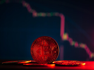 Coins with bitcoin symbol on red light and crypto stocks chart background. Concept of a cryptocurrency market crisis.