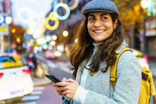 Smiling Hispanic Woman Chatting On Smartphone In Night City