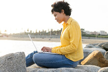Young Man Using Laptop On Rocky Coast