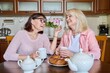 © Valerii Honcharuk - Friends two mature women drinking tea with cupcake in kitchen