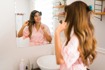 Fototapete - Cheerful woman smiling while doing a curly hairstyle in the bathroom