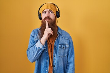 Canvas Print - Caucasian man with long beard listening to music using headphones thinking concentrated about doubt with finger on chin and looking up wondering