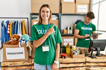 Sticker - Young blonde girl wearing volunteer t shirt at donation stand cheerful with a smile on face pointing with hand and finger up to the side with happy and natural expression