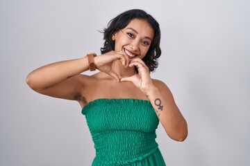 Wall Mural - Young hispanic woman standing over isolated background smiling in love doing heart symbol shape with hands. romantic concept.