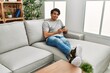 © Krakenimages.com - Young hispanic man using smartphone sitting on the sofa at home.