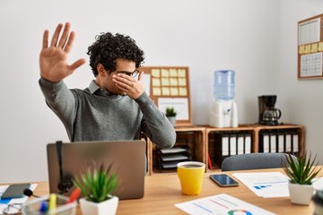 Canvas Print - Young hispanic man wearing business style sitting on desk at office covering eyes with hands and doing stop gesture with sad and fear expression. embarrassed and negative concept.