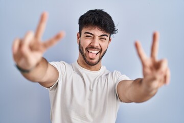 Canvas Print - Hispanic man with beard standing over white background smiling with tongue out showing fingers of both hands doing victory sign. number two.