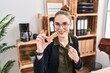 Young hispanic girl eating protein bar as healthy energy snack at the office smiling happy pointing with hand and finger