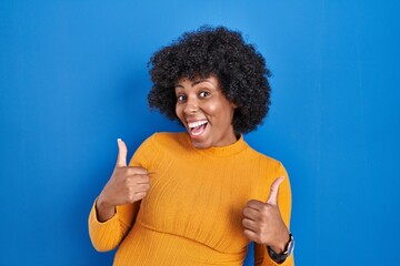 Poster - Black woman with curly hair standing over blue background success sign doing positive gesture with hand, thumbs up smiling and happy. cheerful expression and winner gesture.